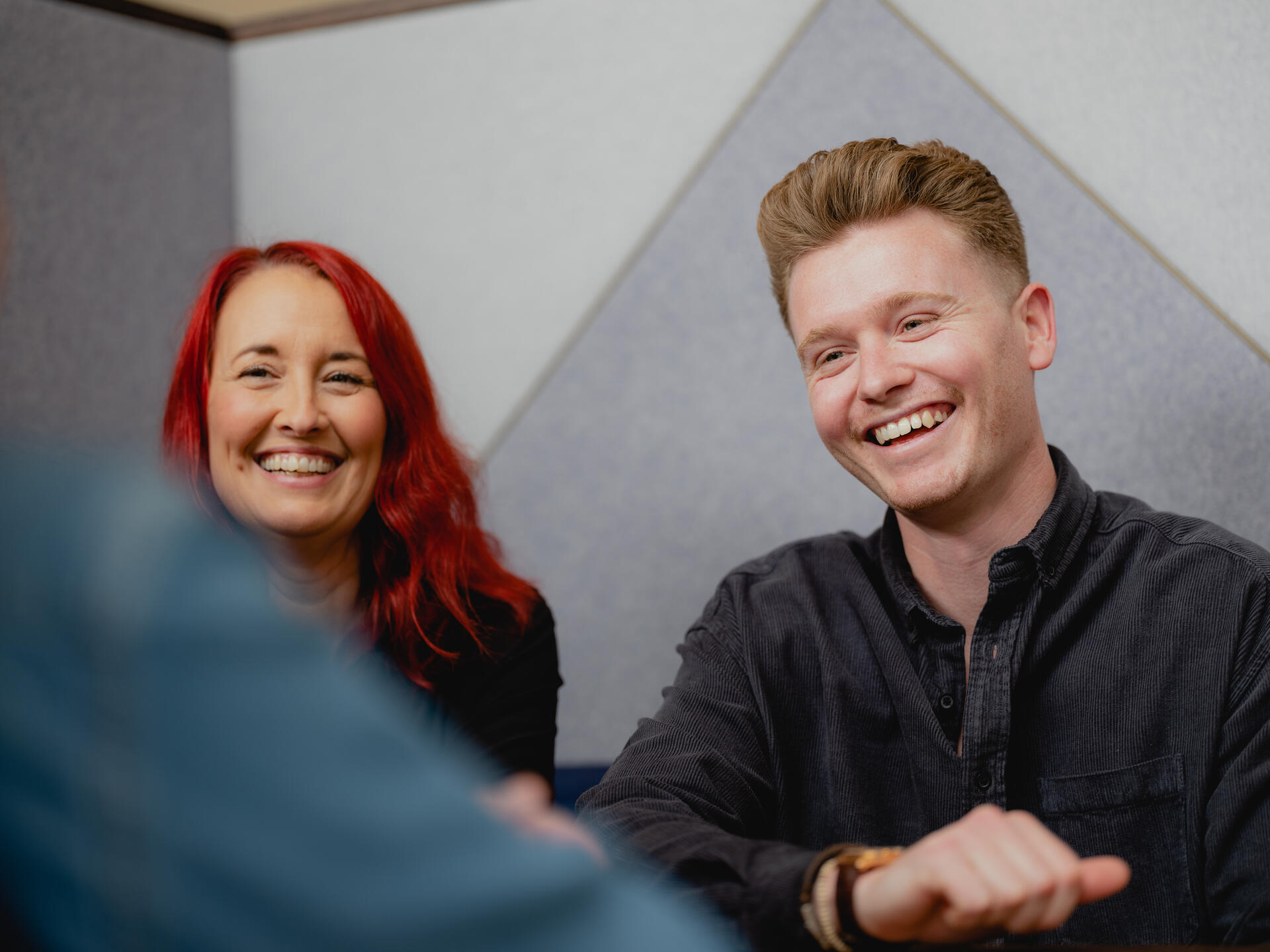 A man and a woman laughing and smiling at a shared desk.